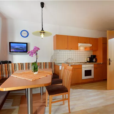 Kitchen with dining area and wood-colored furnishings. A table with chairs and a windowsill with plants are visible.