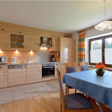 A modern kitchen with wooden cabinets and functional equipment. The table is set, and there are colorful curtains at the window.