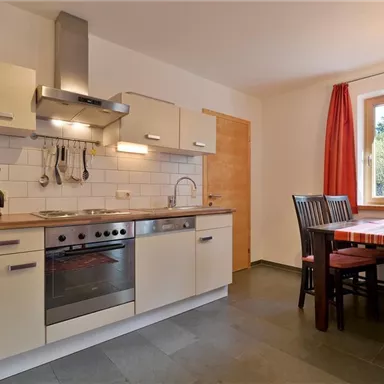 A modern kitchen with a wooden countertop and white cabinets. There are chairs at the table and a window that overlooks greenery.