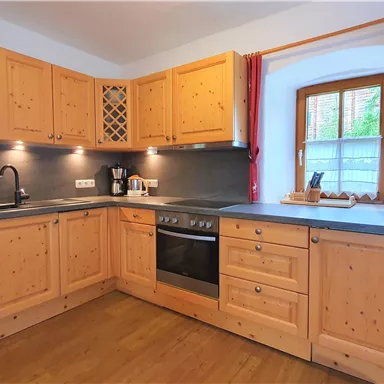 A modern kitchen with wooden cabinets and a dark countertop. There is a sink, a stove, and windows that let in light.