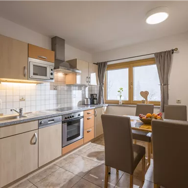 Modern kitchen with wooden furniture and a table for four people. Bright atmosphere due to large windows and daylight.