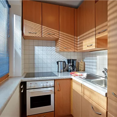 A modern kitchen with wooden cabinets and white tiles. The sun shines through the window and casts shadows on the countertop.