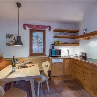 Eine gemütliche Küche mit Holzverkleidungen und moderner Ausstattung. Ein Esstisch mit Stühlen und Fenster, das für Tageslicht sorgt.