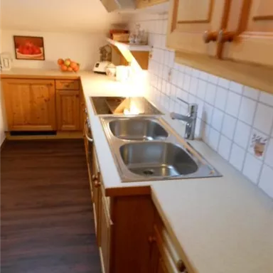 A cozy kitchen with wooden cabinets and a double sink. The countertop is bright and there is pleasant lighting.