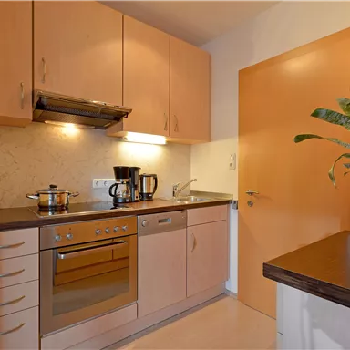 A modern kitchen with wooden cabinets, a stove, and a coffee maker. A pot is boiling on the stove, and a plant is sitting on the countertop.