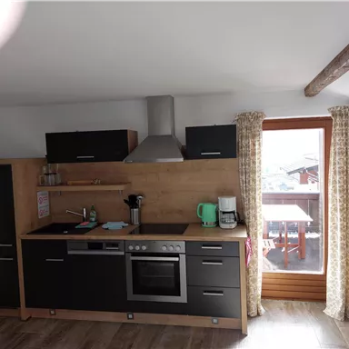 A modern kitchen with wood and black elements. Windows with curtains offer a view outside.