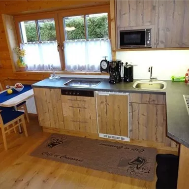 A modern wooden kitchen with a stove, microwave, and sink. There is a small table with chairs and plenty of daylight from the windows.