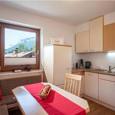 A bright, modern kitchen scene with a dining area and a large window front. The mountains are visible in the background.