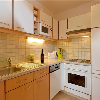 Eine moderne Küche mit Holzschränken, einem Herd und einem Kühlschrank. Sie ist gut ausgestattet mit einem Spülbecken und einer Mikrowelle.