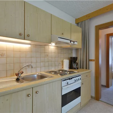 A modern kitchen unit with wooden cabinets and a stove. In the background, there is access to another room.