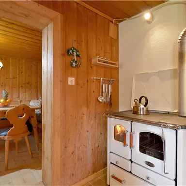 Eine gemütliche Küche mit einer traditionellen Kochstelle und Holzverkleidung. Im Hintergrund ist ein Esstisch mit Stühlen zu sehen.