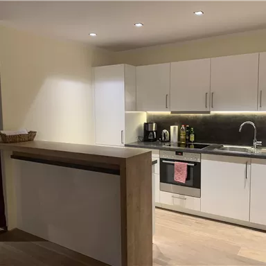 A modern kitchen with white cabinets and a stylish countertop. The equipment includes a stove, a sink, and various household appliances.
