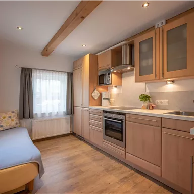 A modern kitchen with wooden cabinets and a light wood floor. The windows let in a lot of daylight.
