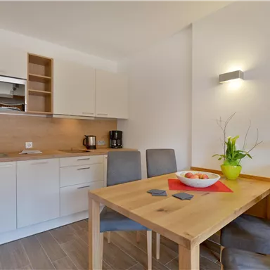 A modern kitchen with a table and chairs. The neutral color scheme and large windows create a friendly atmosphere.