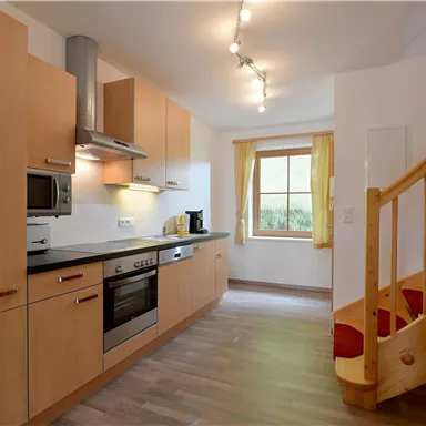 A modern kitchen with wooden cabinets and stainless steel appliances. A staircase leads to an upper floor.