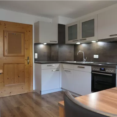 A modern kitchen unit with white furniture and wooden details. The kitchen is well-lit and feels inviting.