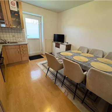 A modern kitchen with a dining area. The table is set and there is a television as well as a door that leads outside.