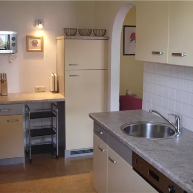 A modern kitchen with bright furniture and a large workspace. The equipment includes a refrigerator, a sink, and a cooking area.