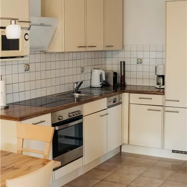 A modern kitchen with light cabinets and a wooden countertop. There is a dining area with a table and chairs.