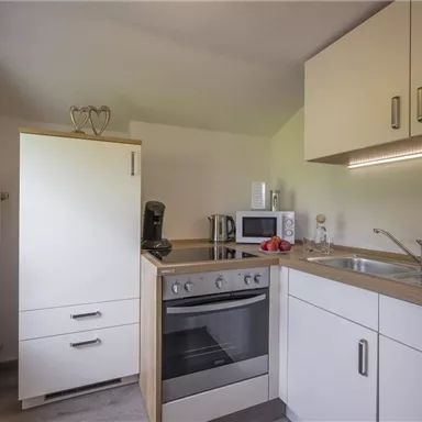 A modern kitchen with white cabinets and a stove. Kitchen utensils and fresh fruit are on the countertop.