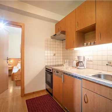 Eine moderne Küche mit Holzschränken und einem hellen Ambiente. Der Raum ist funktional eingerichtet mit Geräten und Stauraum.