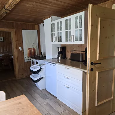 Eine gemütliche Küche mit weißen Schränken und Holzdetails. Im Hintergrund ist ein Essbereich sichtbar.