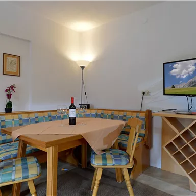 A cozy living area with a dining table and colorful chairs. On the wall, there is a television and a bottle of wine on the table.