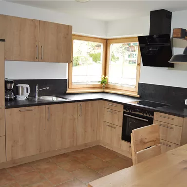 A modern kitchen with wooden cabinets and a black countertop. Plenty of natural light through large windows.