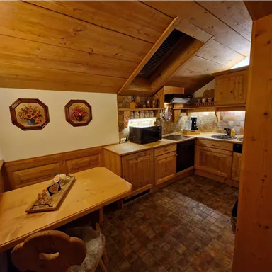 A cozy country-style kitchen with wood paneling and a table. The amenities include a stove, a microwave, and decorative wall pictures.