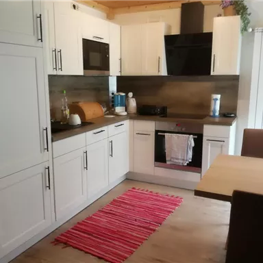Eine moderne Küche mit weißen Schränken und einer Holzarbeitsfläche. Der Tisch ist aus Holz, und ein roter Teppich liegt auf dem Boden.