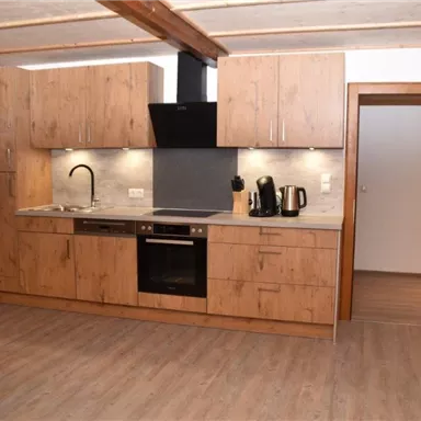 Eine moderne Küche mit Holzmöbeln und einer klaren Arbeitsfläche. Der Raum ist hell und einladend mit einem Essbereich und einem Sofa.