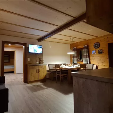 Eine gemütliche Wohnung mit Holzverkleidung und modernen Möbeln. Der Raum ist hell erleuchtet und hat einen Esstisch sowie eine kleine Küche.