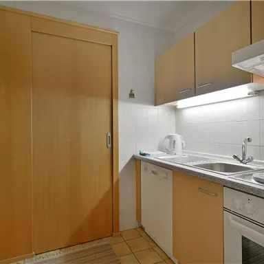 A modern kitchen with light wooden cabinets and a bright countertop. The equipment includes a stove, oven, and sink.