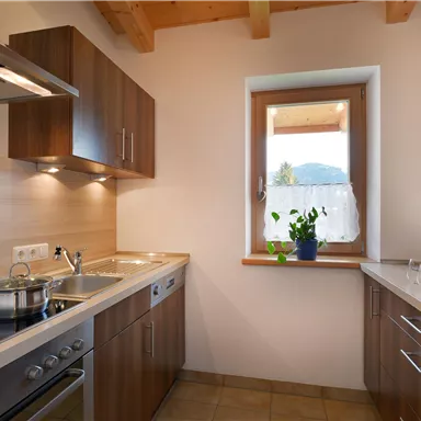 A modern kitchen with wooden cabinets and bright walls. There is a window with a view outside and a cooking area.