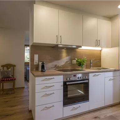 A modern kitchen with white cabinets and hardwood flooring. Light comes through a window, making the space friendly and inviting.