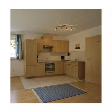 A modern kitchen with light wooden cabinets and a stove. The room is well-lit and has a carpet on the floor.
