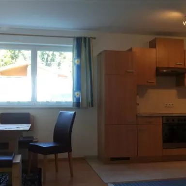 A bright, modern kitchen with a dining area. There is a wooden table and chairs as well as a large window front with a view to the outside.