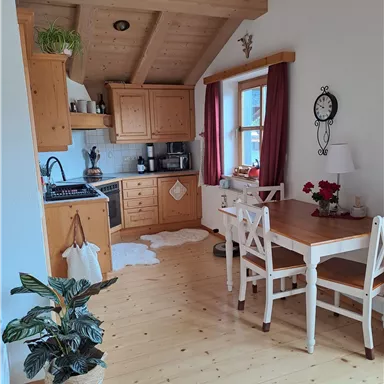 A cozy kitchen with wooden cabinets and a dining table.
Plants and red curtains give the room an inviting atmosphere.