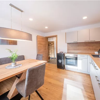 A modern kitchen with a dining area and a wooden table. The walls are bright and the furniture is stylishly arranged.