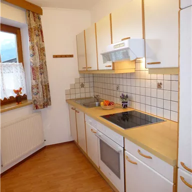 A modern kitchen with white cabinets and wooden details. There is a stove, a sink, and fruit on the countertop.