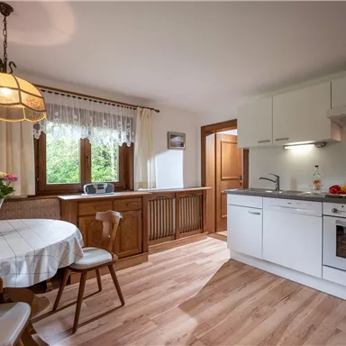 A bright kitchen with a round table, chairs, and modern amenities. Large windows let in plenty of light and offer a view of the greenery.