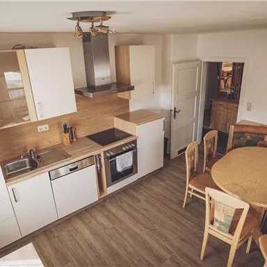 Eine moderne Küche mit weißen Schränken und Holzdetails. Der Essbereich verfügt über einen runden Tisch und gepolsterte Sitzbänke.