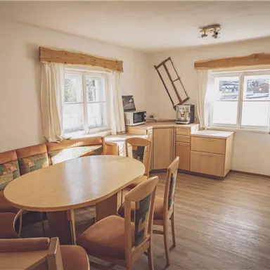 Eine gemütliche Küche mit einem runden Tisch und einer Eckbank. Große Fenster sorgen für viel Licht und eine einladende Atmosphäre.