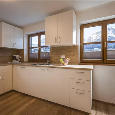 A modern kitchen with white cabinets and wood paneling. Large windows provide a view of the mountains.