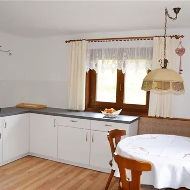 A bright kitchen with modern furniture and a cozy dining area. The table is covered with a white tablecloth and there is fresh fruit in a bowl.