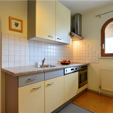 A modern kitchen with bright cabinets and a stove. In the background, there is a dining area with wooden chairs.