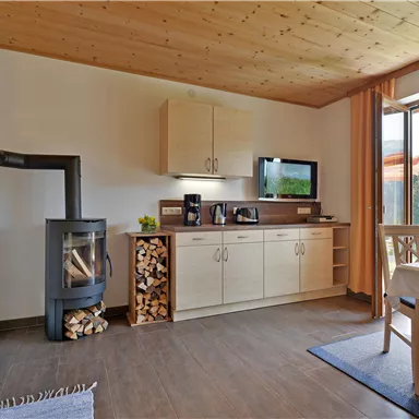 A modern kitchen with light wood cabinets and a dining area. A fireplace and large windows create a cozy atmosphere.