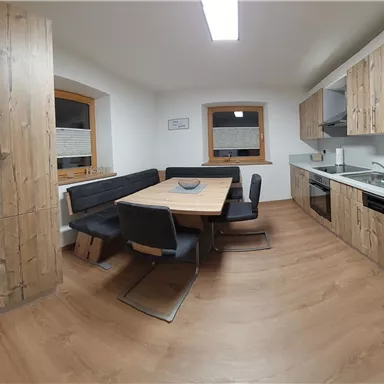 Eine moderne Küche mit Holzschränken und einem großen Esstisch. Der Raum ist hell und einladend gestaltet.