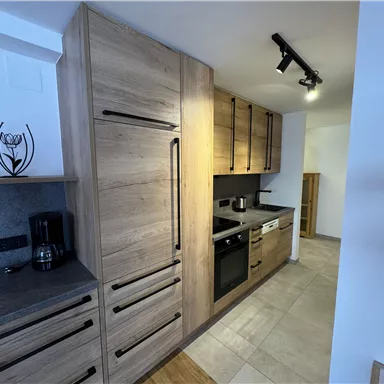 A modern kitchen with wooden cabinets and gray countertops. The equipment includes a refrigerator, a stove, and a sink.