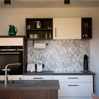 Eine moderne Küche mit Holz- und weißen Schränken. Die Wand ist mit einer grauen, gemusterten Fliese dekoriert.